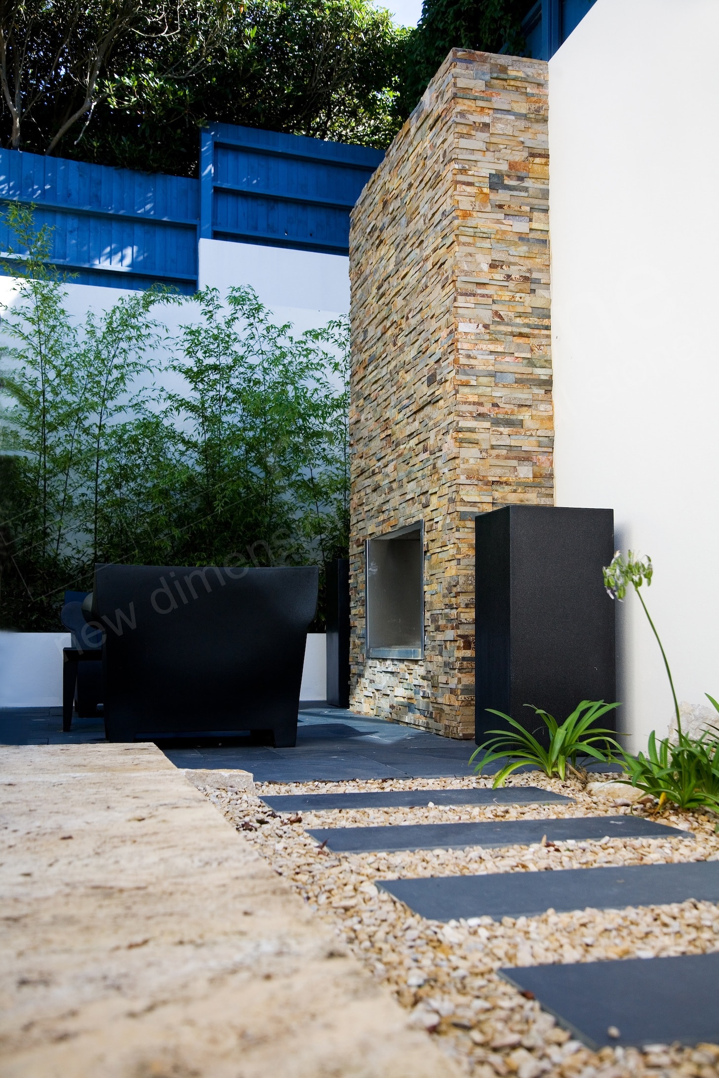A large two story outdoor fireplace clad with stone veneer and a stainless steel firebox